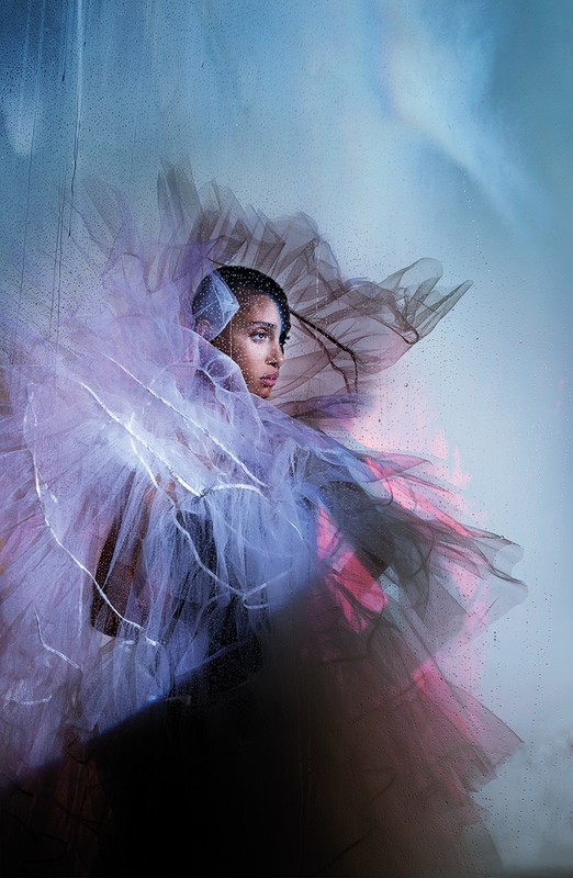 Artistic portrait of a woman with short hair wearing a layered tulle gown against a misty blue background in an indoor studio setting.