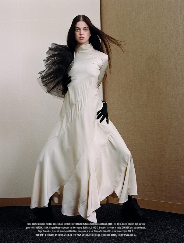 Model in long white dress with black tulle shoulder detail wearing black gloves against a paneled background