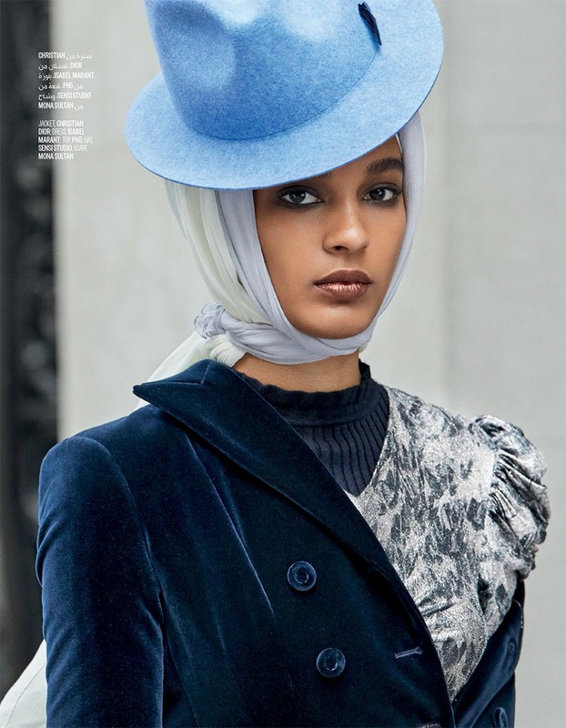 Woman in blue velvet jacket and blue hat poses indoors. She is wearing a white headscarf and a silver patterned blouse.