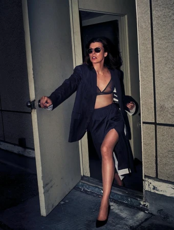 Woman wearing sunglasses and a dark suit jacket opening a door outdoors at night styled by Anya Ziourova