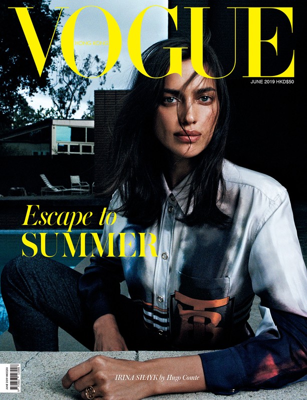 Vogue magazine cover featuring Irina Shayk in a button-down shirt and dark jeans, posing near a pool with a modern house in the background.