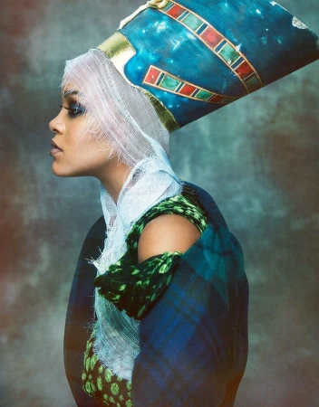 Profile portrait of a woman wearing a tall blue headdress, white netting over her hair, and a dark plaid coat with green accents.