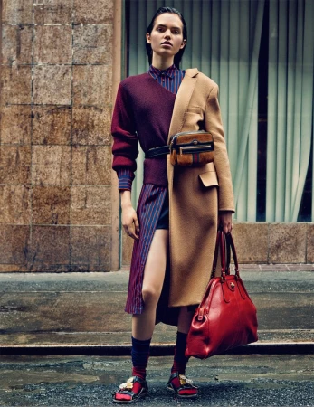 Model standing outdoors wearing a mixed burgundy sweater coat and tan jacket styled by Anya Ziourova.