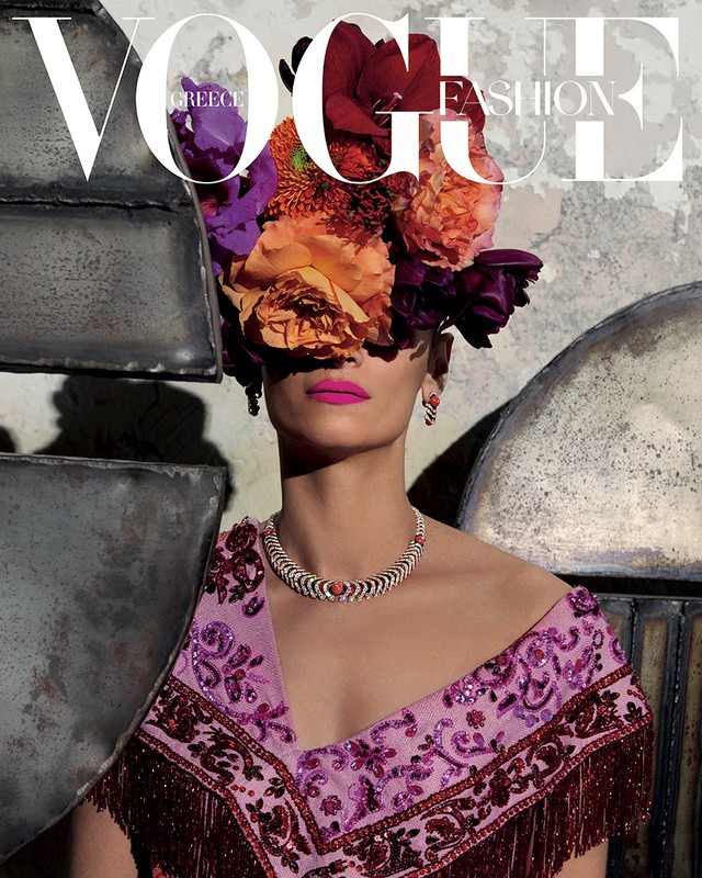 Vogue Greece cover featuring an adult female model adorned with bright flowers, statement jewelry, and magenta lipstick.
