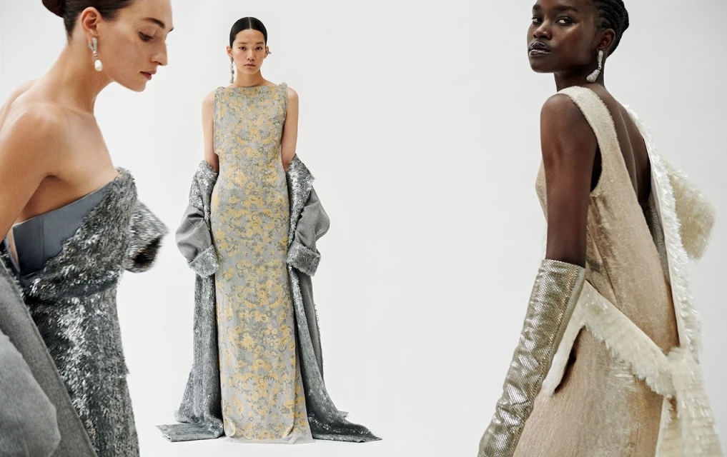Three women in evening gowns and shimmering coats pose against a white backdrop, showcasing elegant formal wear in a studio setting.