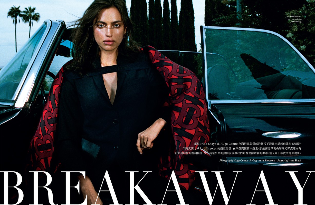 Irina Shayk poses in a black jacket with patterned sleeves next to a black vintage convertible car in an outdoor editorial fashion shot.