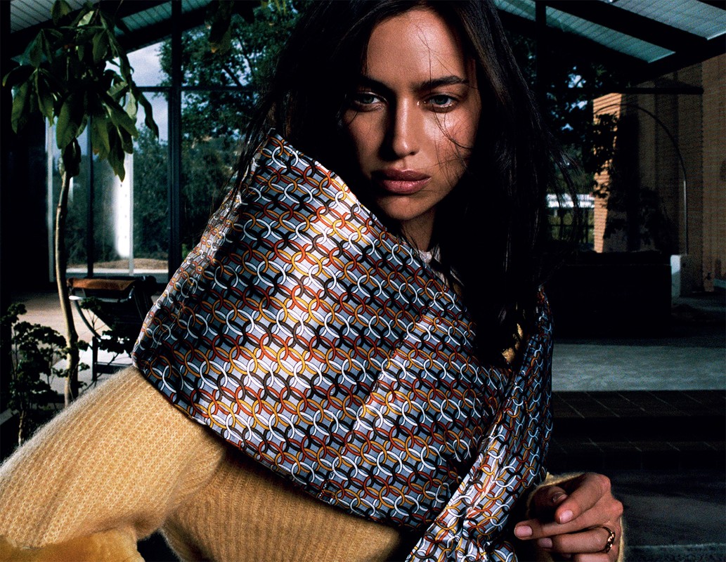 Model Irina Shayk wearing a patterned silk scarf and yellow knit sweater inside a modern home interior.