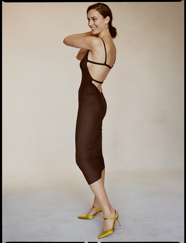 Woman in a backless brown dress and yellow heels posing in a photo studio. Fashion shot of a slender adult female model.