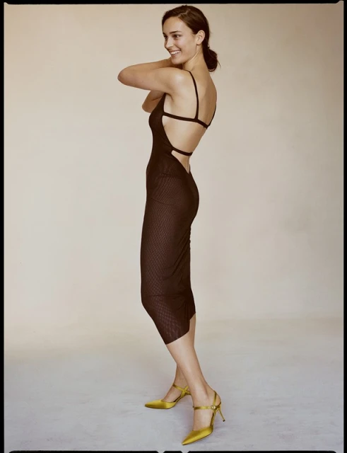 Woman in a backless brown dress and yellow heels posing in a photo studio. Fashion shot of a slender adult female model.
