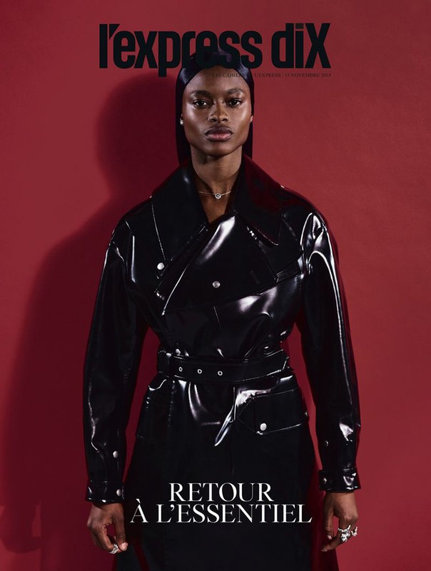 Magazine cover featuring an African American woman with a serious expression wearing a black vinyl trench coat against a red background.