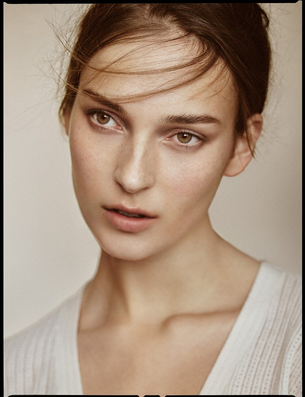 Close-up portrait of a woman with light brown hair and natural makeup wearing a white top