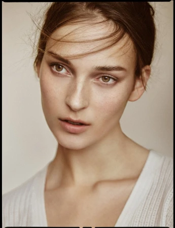 Close-up portrait of a woman with light brown hair and natural makeup wearing a white top