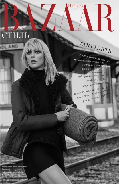 Black and white fashion editorial featuring a fair-skinned woman with blonde hair in a dark outfit holding a blanket, outdoors.
