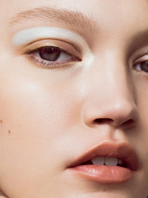 Close-up beauty portrait of an adult female with light skin, light eyebrows, and light-colored eyeshadow, glossy lips, and visible pores.