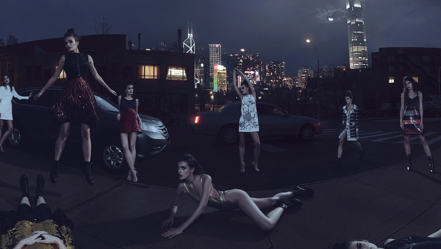 Fashion photo shoot featuring multiple adult female models in short dresses, posing outside at night with cars and a city skyline in the background.