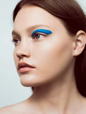 Close up portrait of a young woman with vibrant blue eyeshadow and natural makeup against a plain background