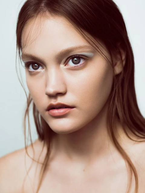 Close-up studio shot of a young adult female with long brown hair and light skin tone, wearing pale eyeshadow. Beauty shot, portrait.