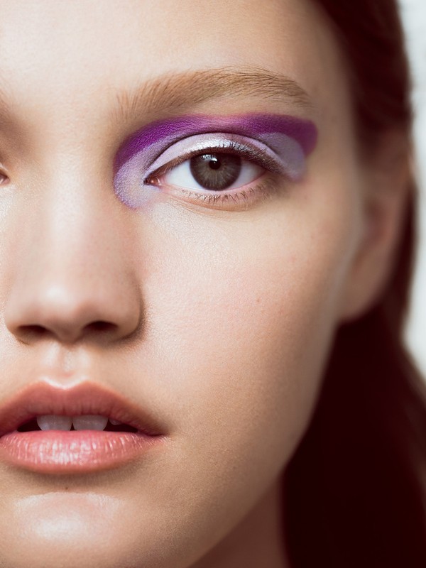 Close-up portrait of a woman wearing bold purple and lavender eye makeup with a silver metallic accent line.