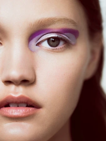 Close-up portrait of a woman wearing bold purple and lavender eye makeup with a silver metallic accent line.