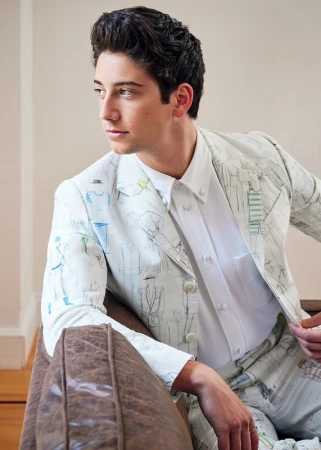 Young man in illustrated print suit jacket and white shirt seated indoors in Los Angeles