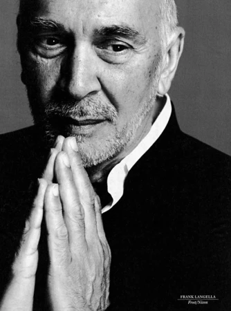 Black and white portrait of mature man with beard in suit with hands together in prayer or thoughtful pose, looking at camera.