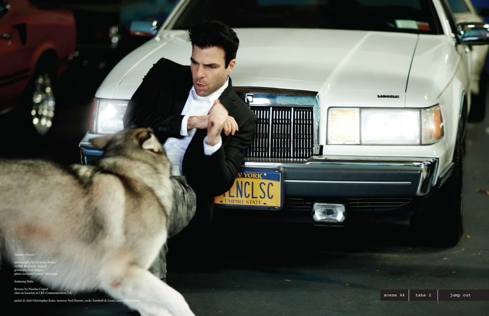 Zachary Quinto poses with a husky dog near a vintage white Lincoln car. The image is taken outdoors, set against a dark parking lot.