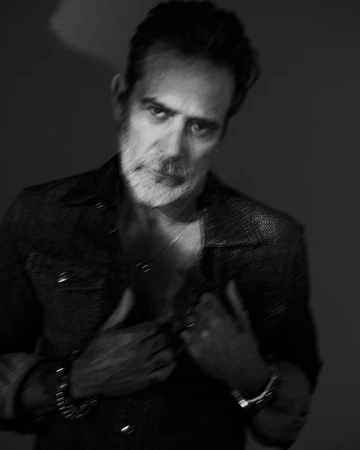 Black and white portrait of an adult male with grey hair and beard in an open button-down shirt holding its sides.