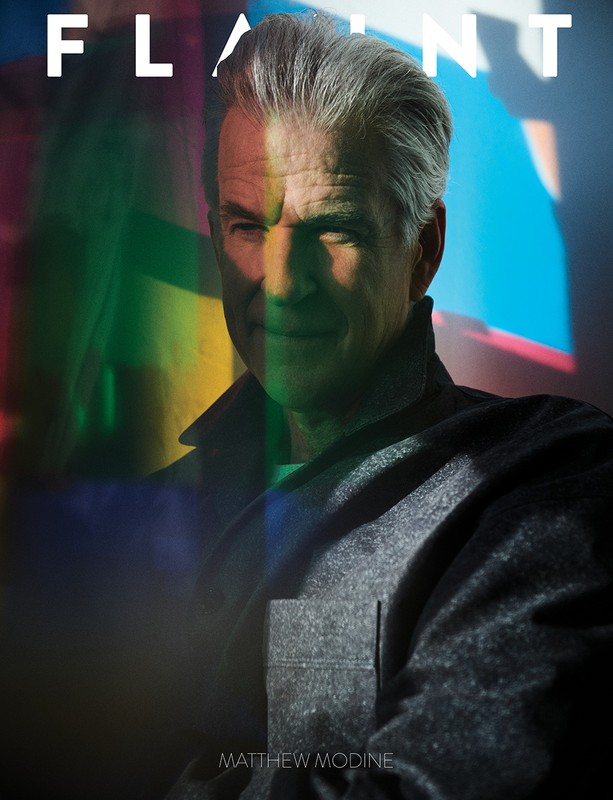 Matthew Modine portrait on FLAUNT magazine cover with gray jacket, short gray hair, and dramatic lighting with colorful prism effects.