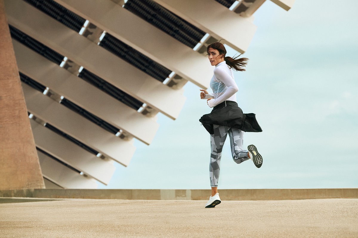 Athletic woman running outdoors near an abstract, modern building with a black jacket tied around her waist. Fitness concept.