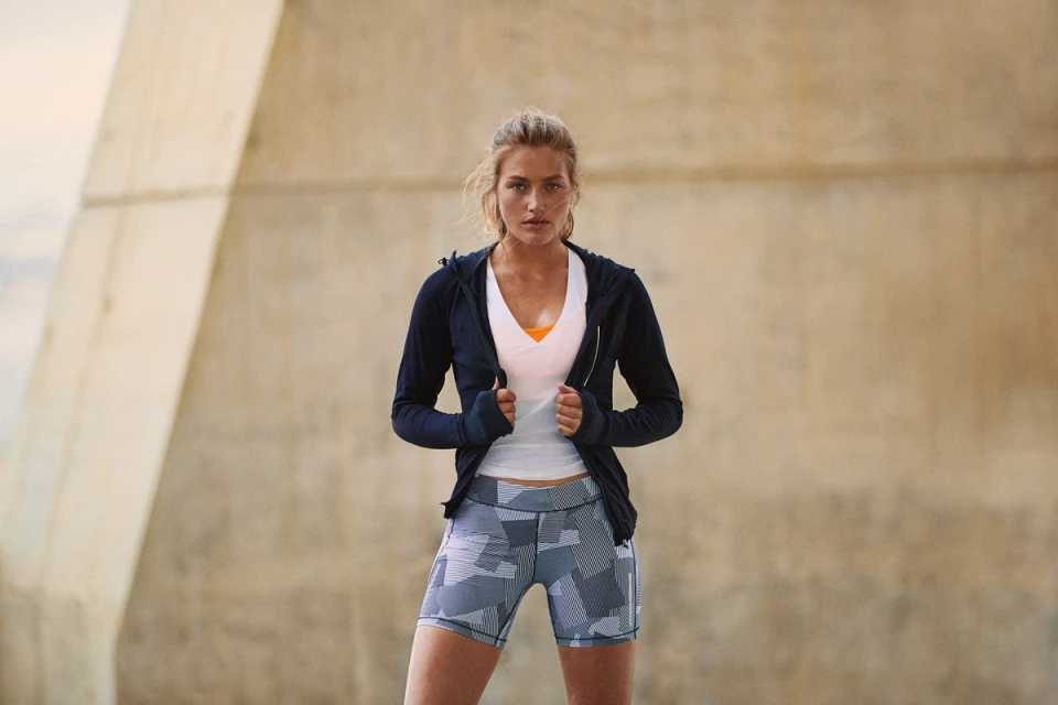 Athletic woman poses in black jacket and patterned shorts outdoors. Fitness lifestyle image showcasing activewear and healthy living.