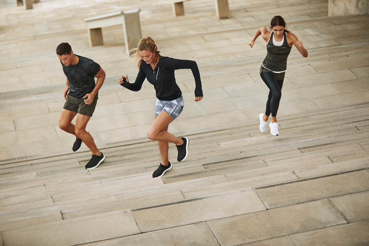 Three people, two women and one man, are running up a long flight of concrete stairs outdoors during the daytime, focusing on fitness.