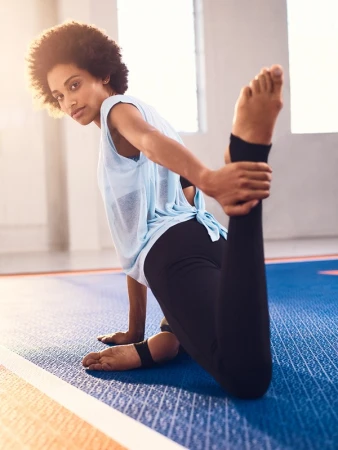 Woman with afro hair wearing a light blue top and black leggings stretching in a gym, photographed by Bersa.