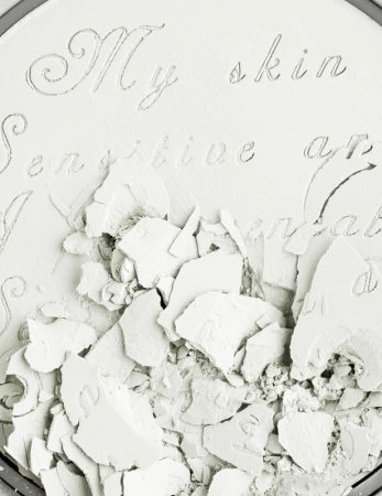 Close-up of crushed white powder inside a round container, with embossed text that reads 'My skin sensitive and comfortable'.