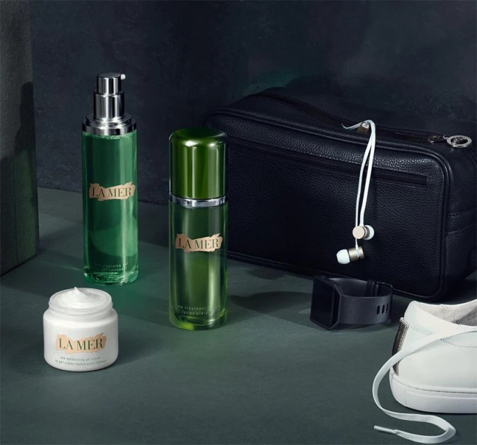 Still life of La Mer skincare products including creams, serum, and lotion, along with a black travel bag, smart watch, and white sneakers.