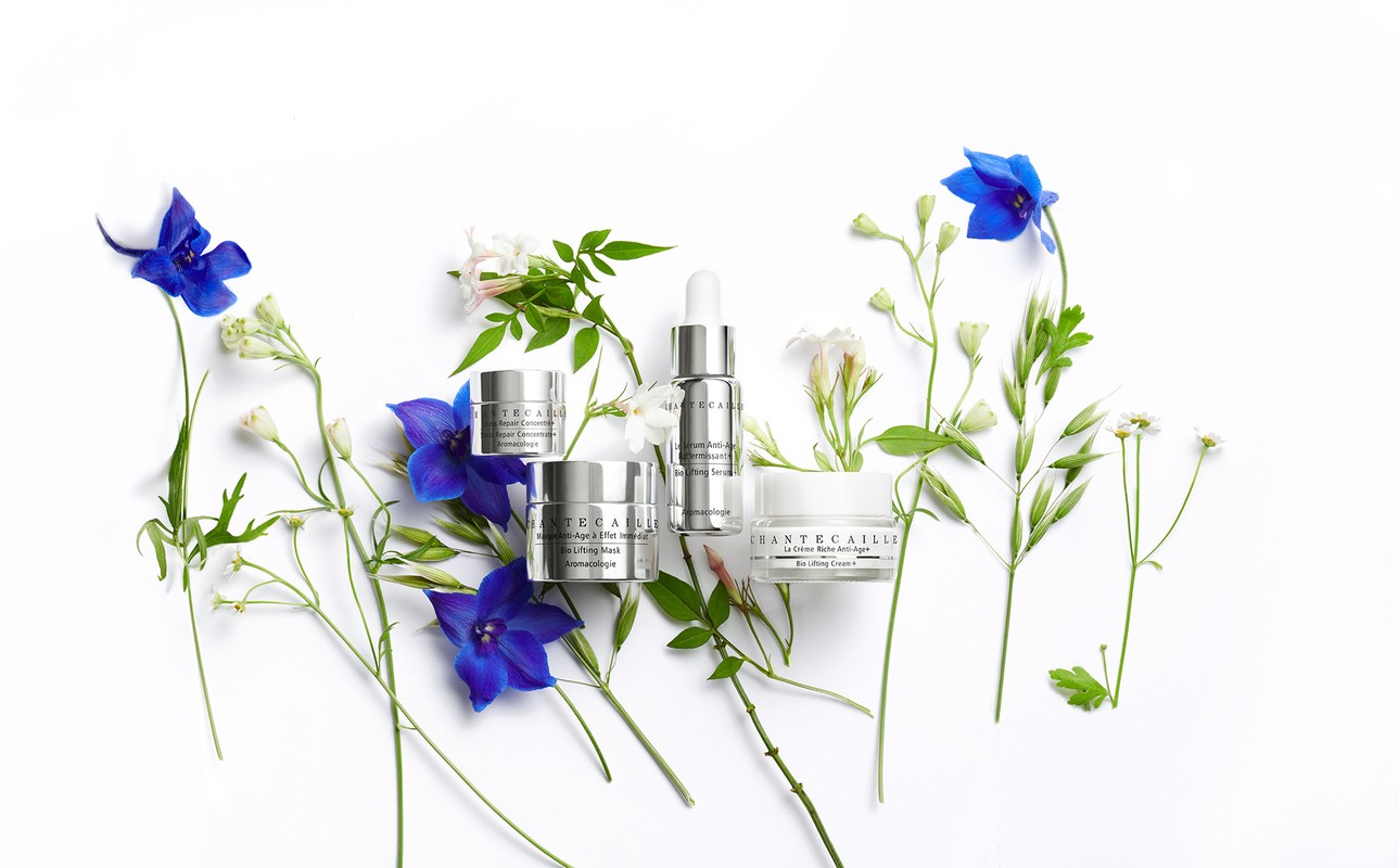 Chantecaille skincare products, including face cream and serum, arranged with assorted blue and white flowers on a white background.