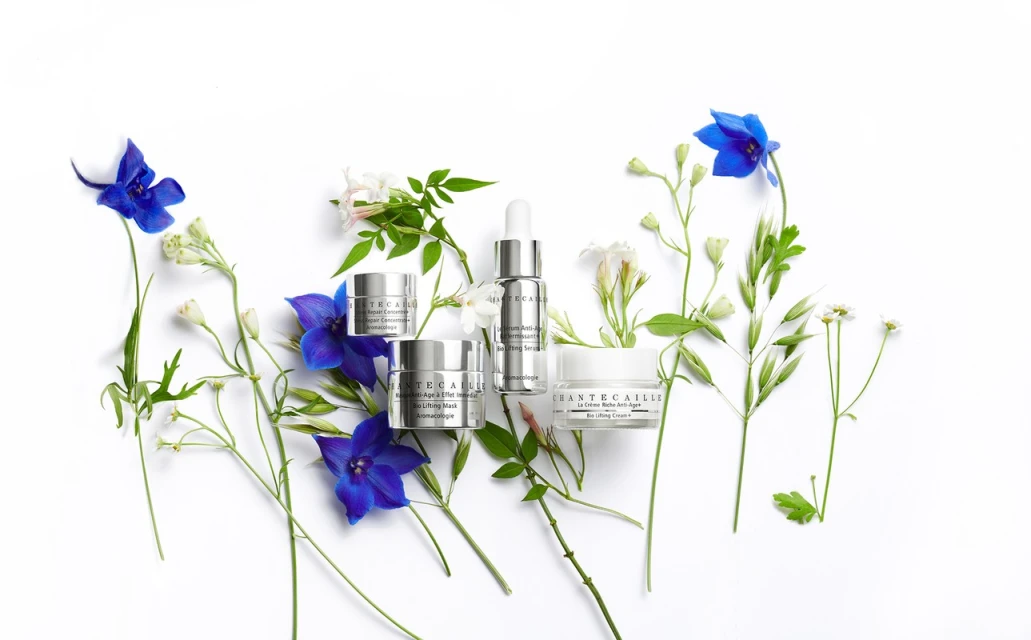 Chantecaille skincare products, including face cream and serum, arranged with assorted blue and white flowers on a white background.
