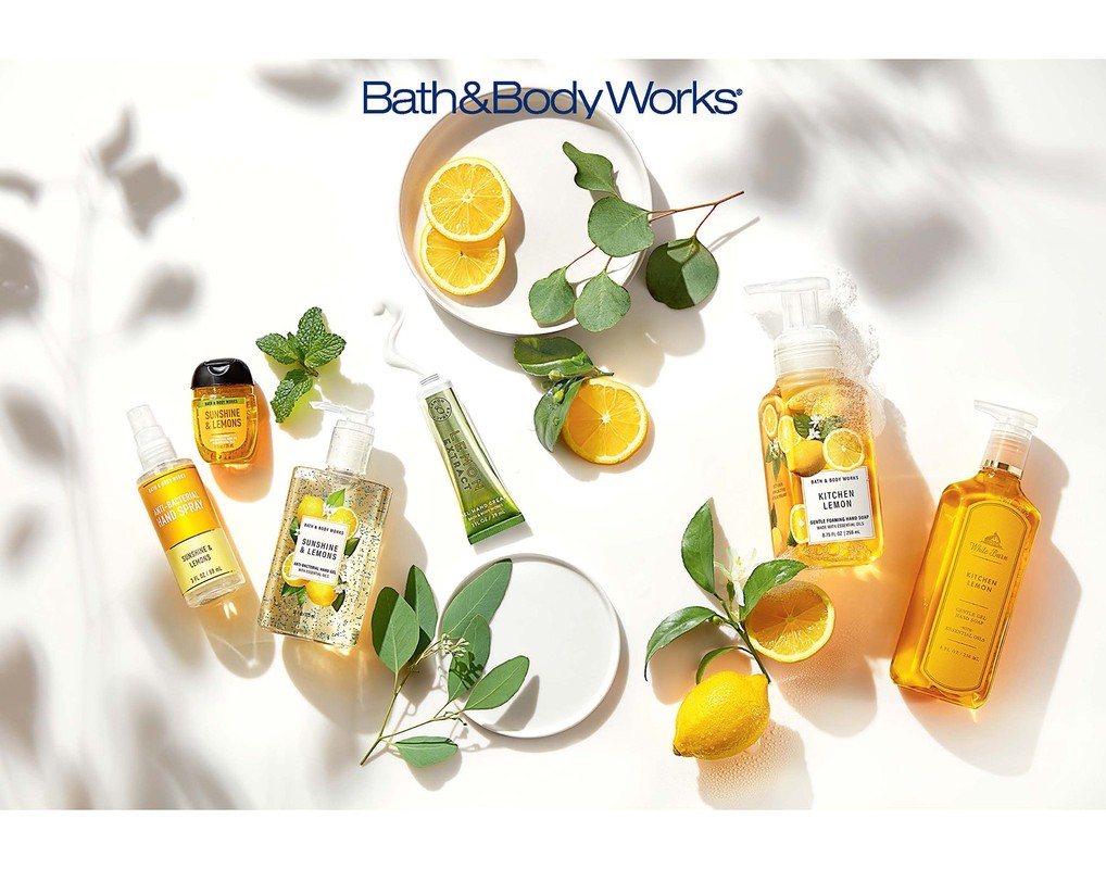 Bath & Body Works lemon-themed products displayed with lemons and greenery on a white surface with shadow patterns overhead.