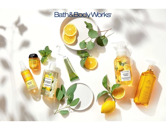 Bath & Body Works lemon-themed products displayed with lemons and greenery on a white surface with shadow patterns overhead.