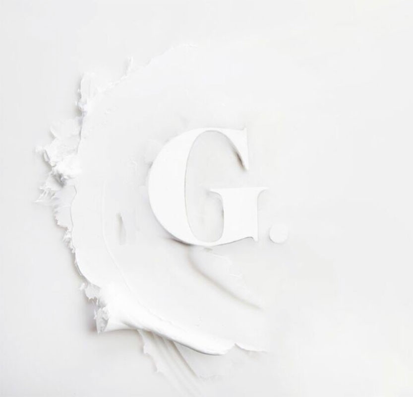 Letter G formed with white cosmetic cream, showcasing a smooth, even texture, and minimalist beauty concept on a plain white background.