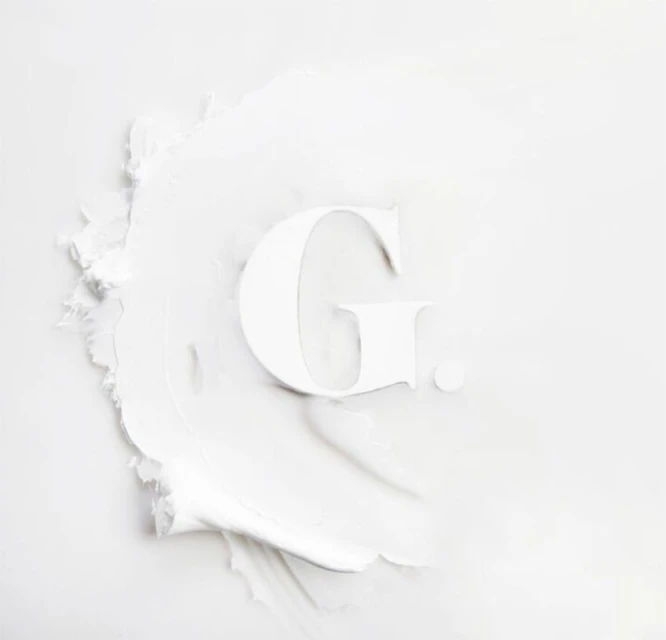 Letter G formed with white cosmetic cream, showcasing a smooth, even texture, and minimalist beauty concept on a plain white background.
