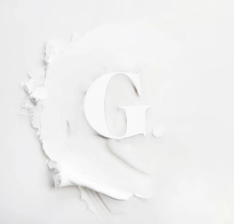Letter G formed with white cosmetic cream, showcasing a smooth, even texture, and minimalist beauty concept on a plain white background.