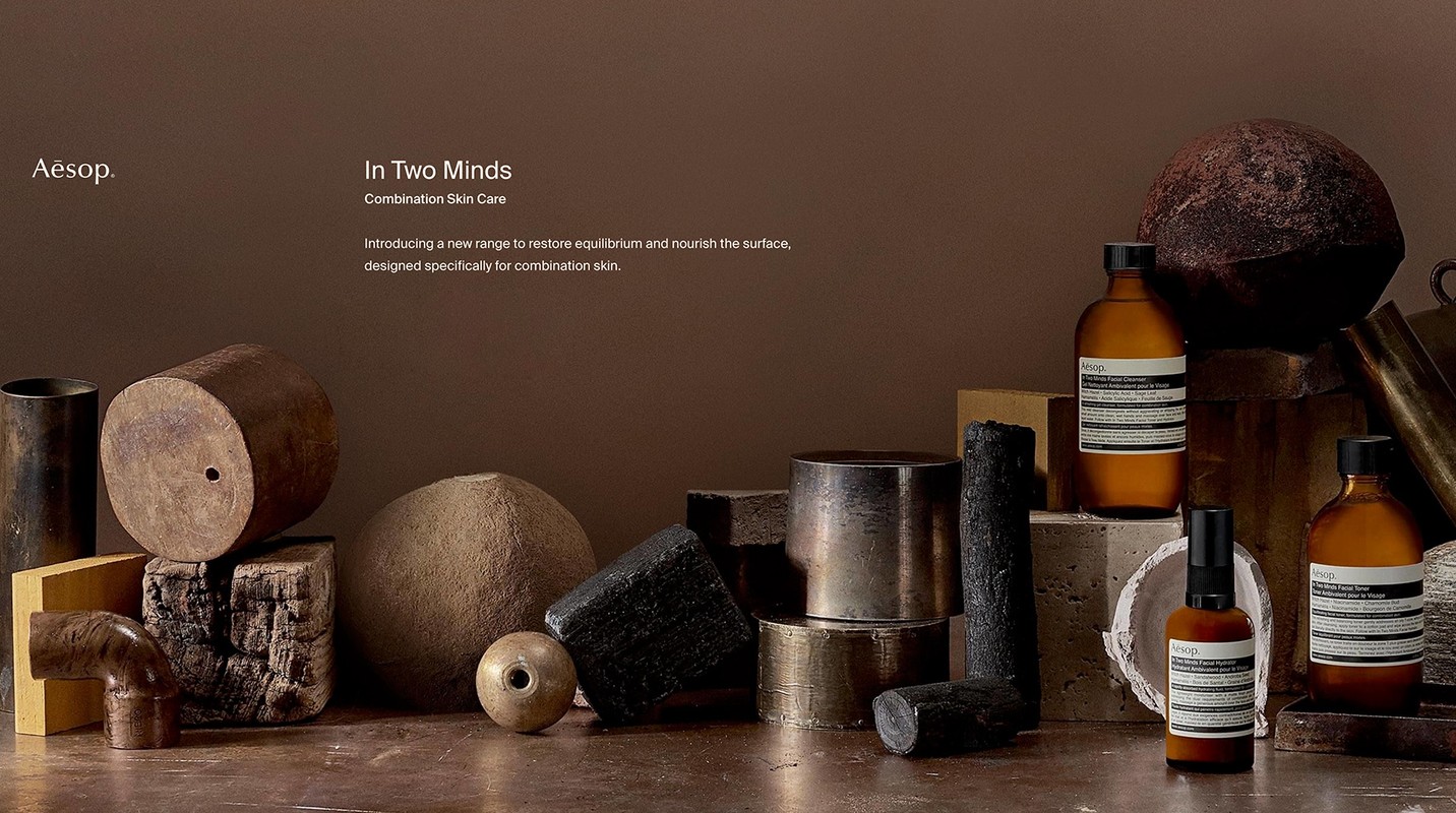 Still life of Aesop skincare products, including bottles and jars, arranged with various geometric shapes and natural textures, set against a brown backdrop.