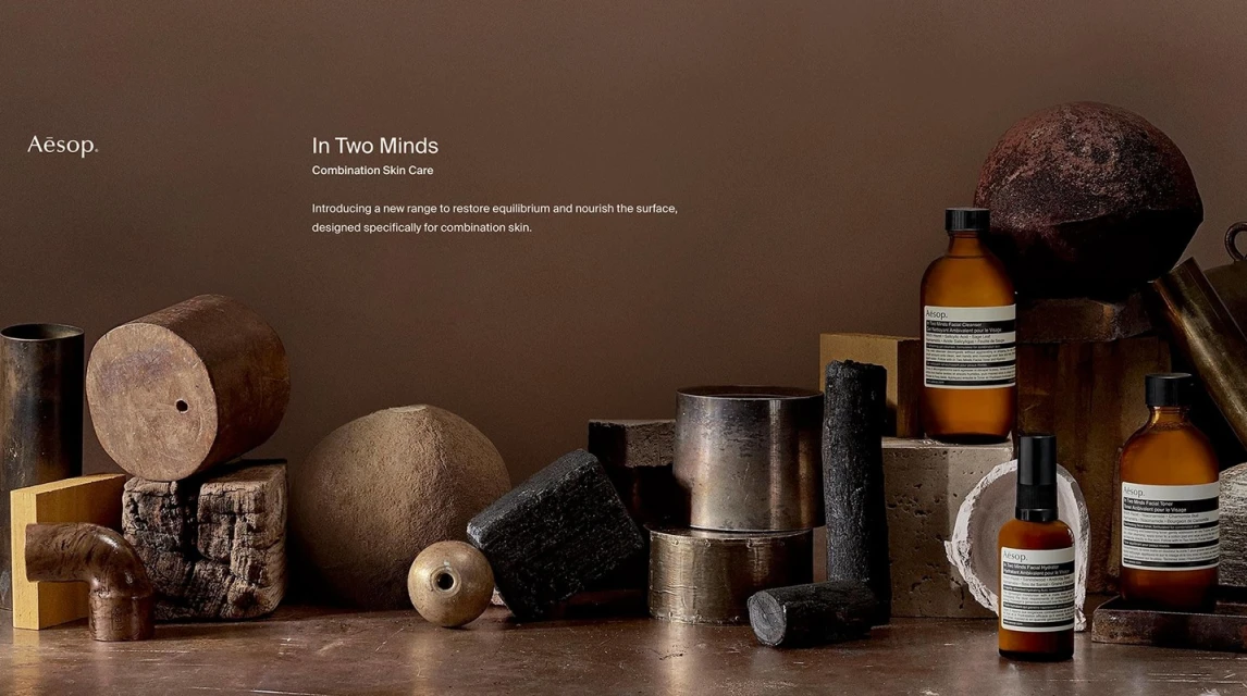 Still life of Aesop skincare products, including bottles and jars, arranged with various geometric shapes and natural textures, set against a brown backdrop.