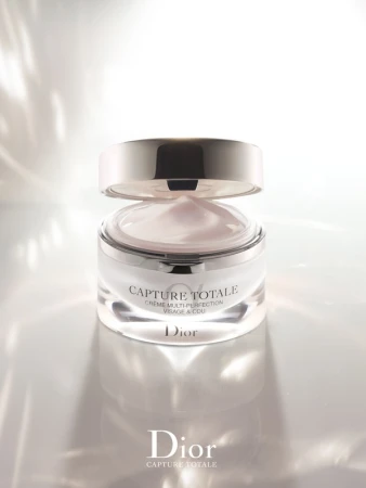 Close-up of a jar of Dior Capture Totale cream with its silver lid slightly ajar, set against a bright, neutral studio background.