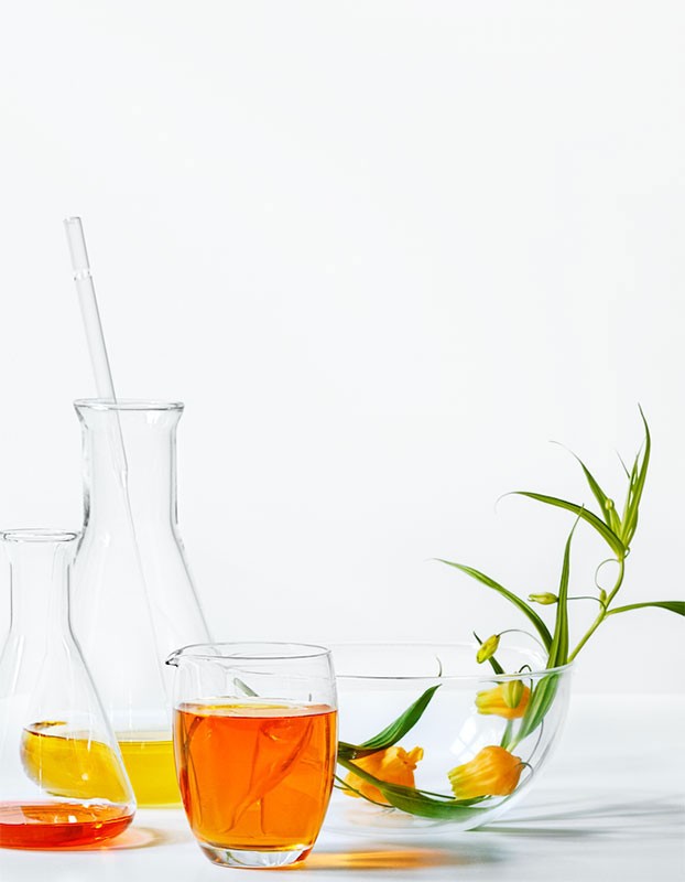 Laboratory glassware including beakers and flasks filled with orange and yellow liquids, alongside flowers in a clear bowl.