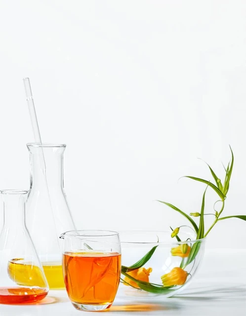 Laboratory glassware including beakers and flasks filled with orange and yellow liquids, alongside flowers in a clear bowl.