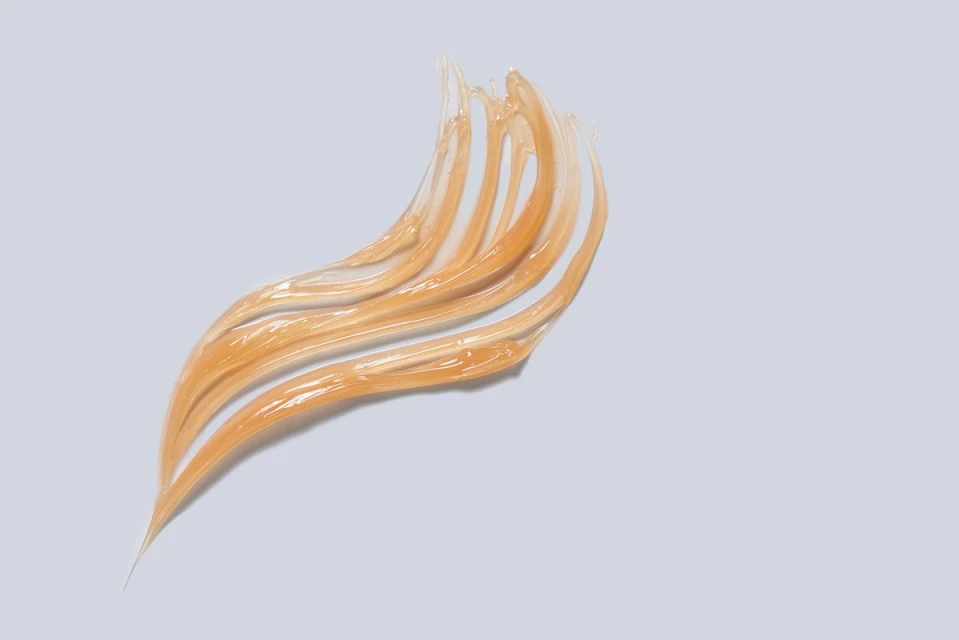 Close-up of a golden gel smear or sample in a curving shape on a plain background, showcasing beauty or skincare product texture.