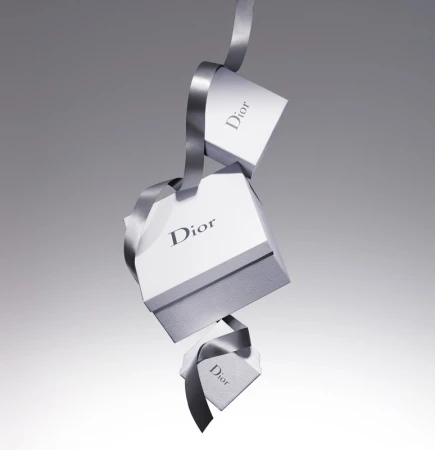 Three Dior branded gift boxes cascade down in a studio shot, connected by a luxurious gray ribbon against a gradient gray background.