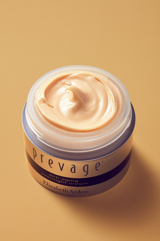 Open cosmetics jar filled with textured peach face cream against a solid warm beige background.