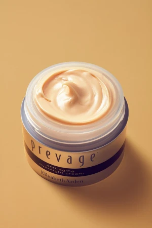 Open cosmetics jar filled with textured peach face cream against a solid warm beige background.